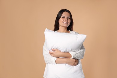 Happy young woman hugging soft pillow on beige background