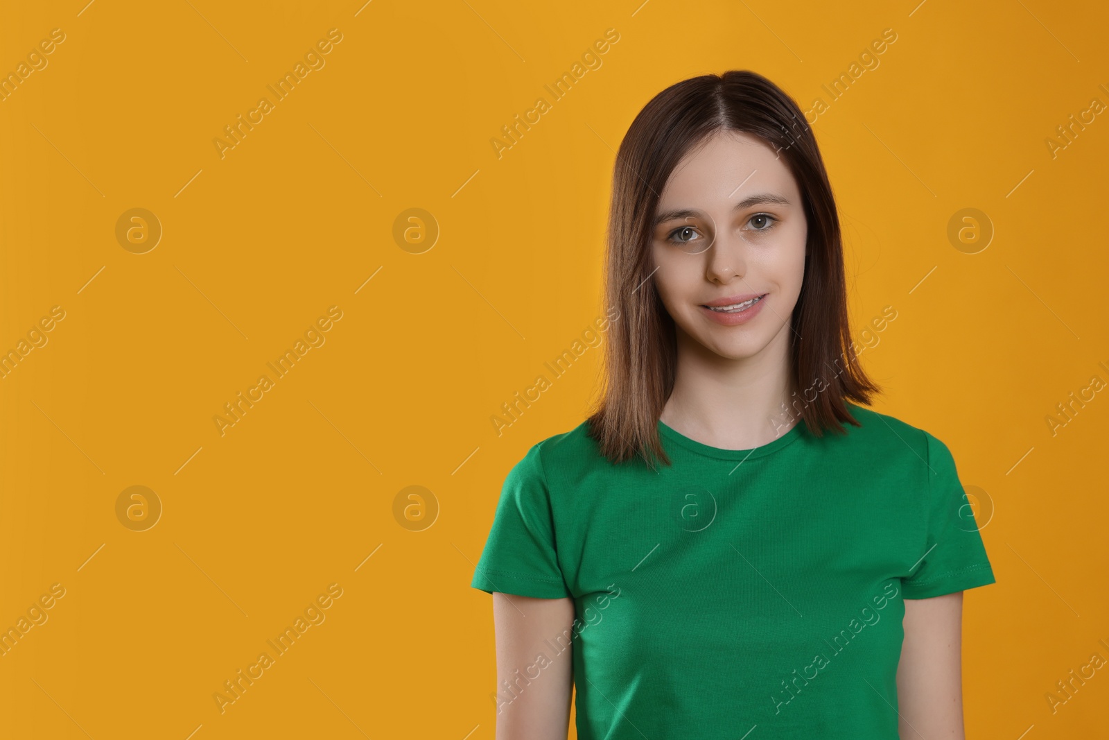 Photo of Portrait of smiling teenage girl on orange background. Space for text