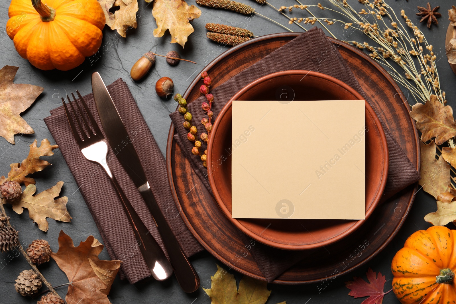 Photo of Festive table setting with blank card, pumpkins and other autumn decor on dark grey background, flat lay. Thanksgiving Day celebration