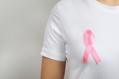 Photo of Woman with pink ribbon on grey background, space for text. Breast cancer awareness