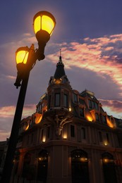 Photo of Glowing streetlight near beautiful illuminated building in evening, low angle view
