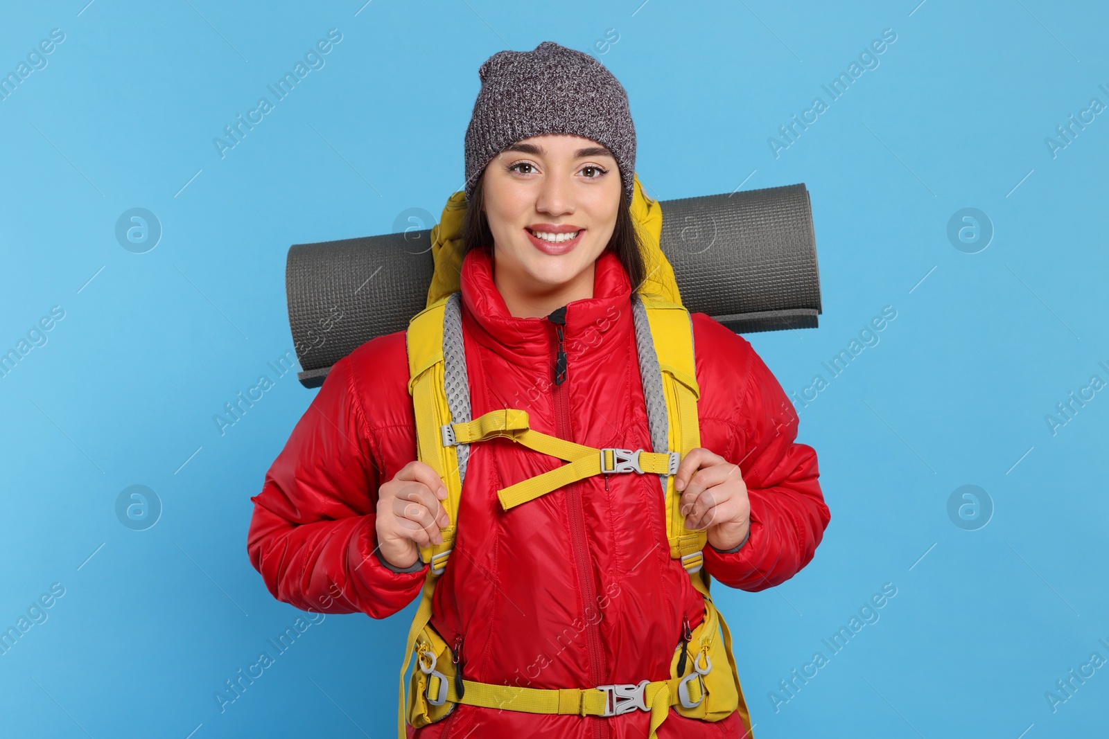 Photo of Smiling young woman with backpack on light blue background. Active tourism
