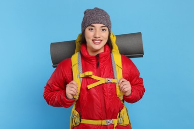 Smiling young woman with backpack on light blue background. Active tourism