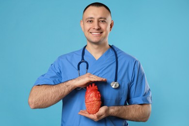 Photo of Doctor with stethoscope and model of heart on light blue background. Cardiology concept
