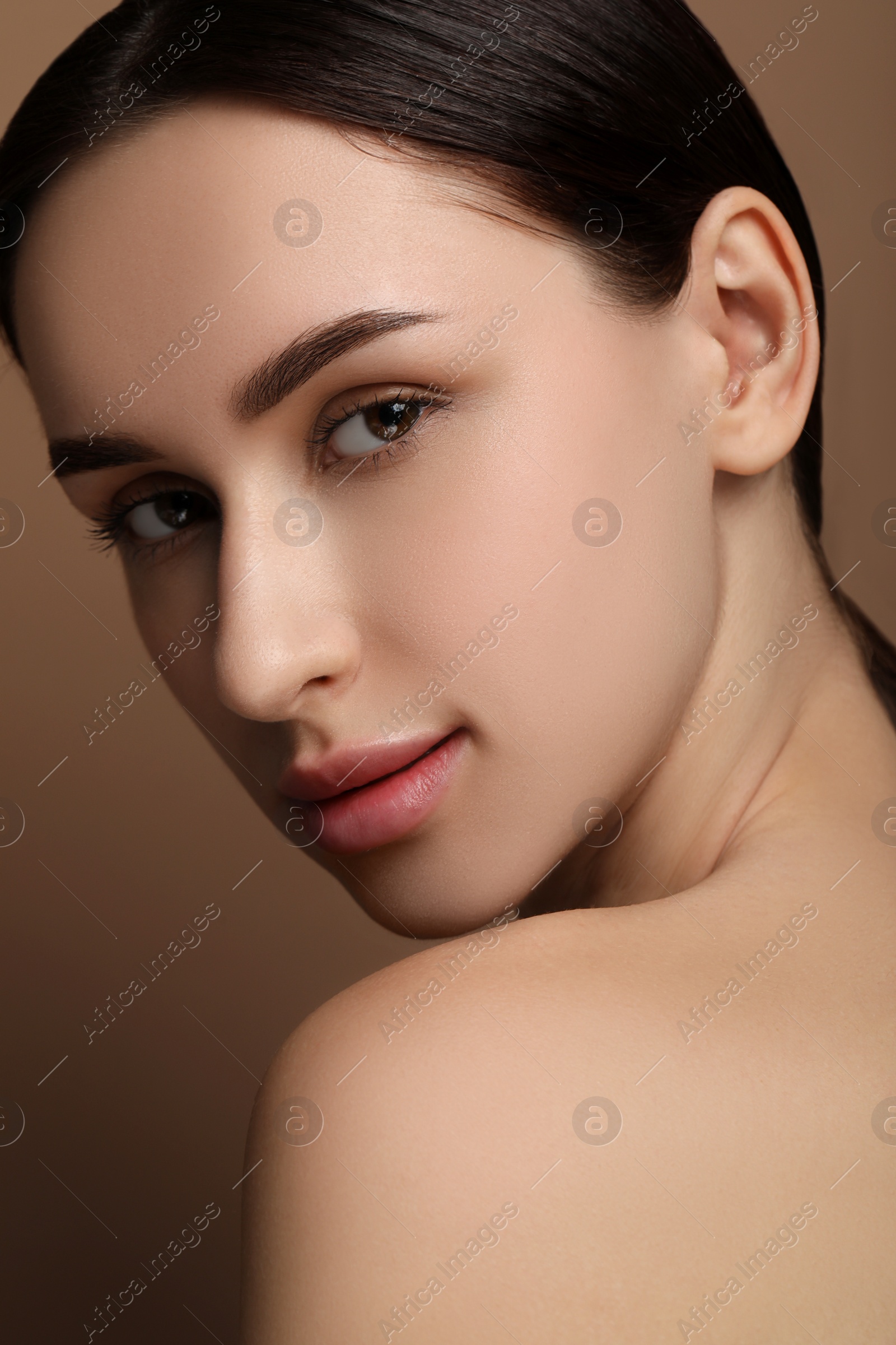 Photo of Beautiful young woman with healthy skin on brown background