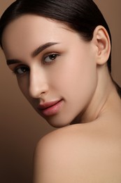 Photo of Beautiful young woman with healthy skin on brown background