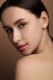 Beautiful young woman with healthy skin on brown background