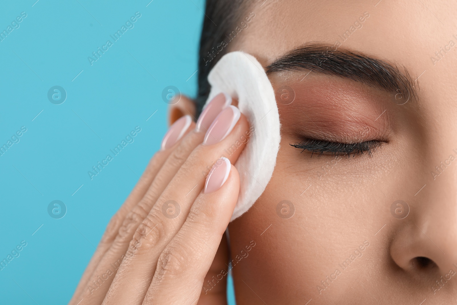 Photo of Beautiful woman removing makeup with cotton pad on light blue background, closeup. Space for text