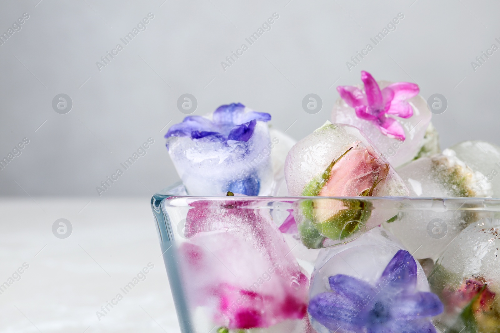 Photo of Glass bowl with floral ice cubes on light background, closeup. Space for text