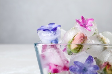 Glass bowl with floral ice cubes on light background, closeup. Space for text