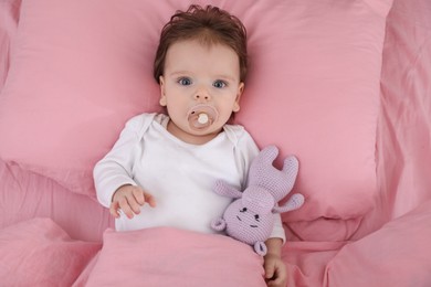 Cute little baby with pacifier and toy on bed, top view