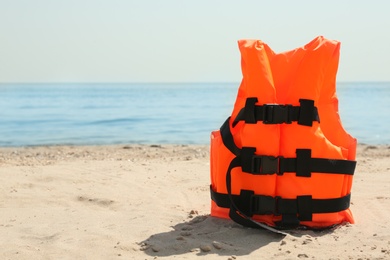Photo of Orange life jacket on sandy beach near sea. Emergency rescue equipment