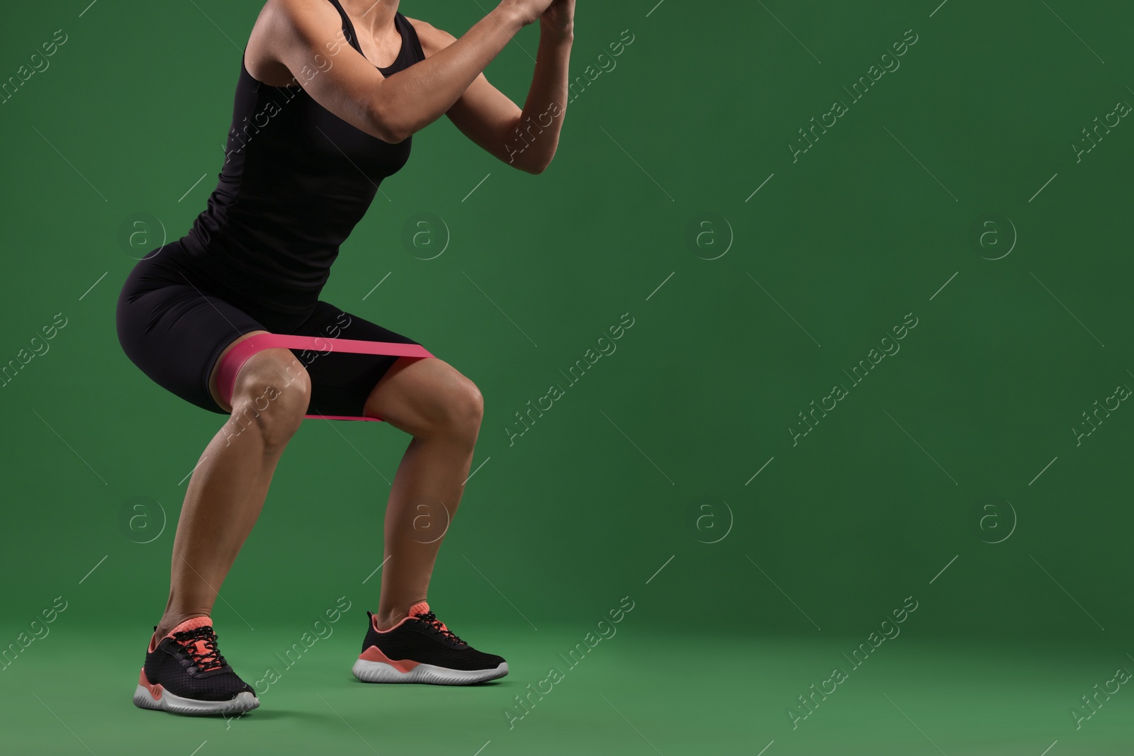 Photo of Woman exercising with elastic resistance band on green background, closeup. Space for text