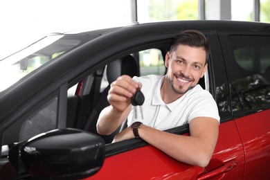 Photo of Happy man with car key sitting in driver's seat of new auto