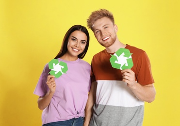 Young couple with recycling symbols on yellow background