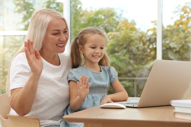 Photo of Happy grandmother and her granddaughter having video chat via laptop together at home