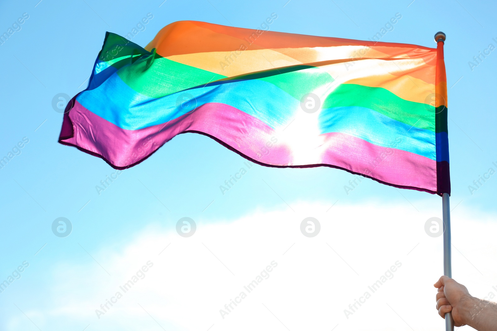 Photo of Gay man holding rainbow LGBT flag against blue sky