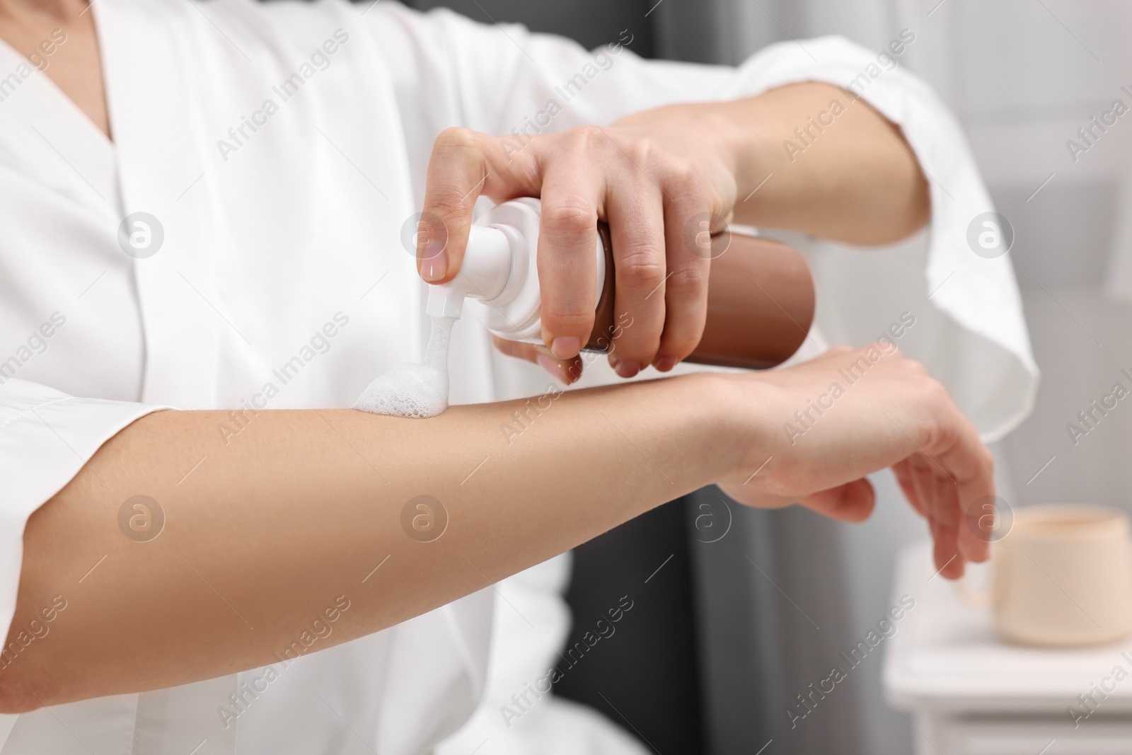 Photo of Woman applying self-tanning product onto arm indoors, closeup