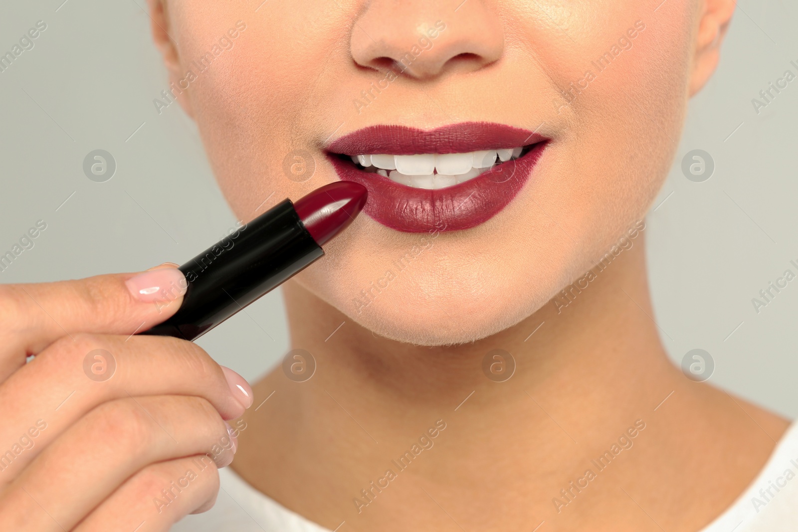 Photo of Beautiful woman applying dark lipstick on gray background, closeup