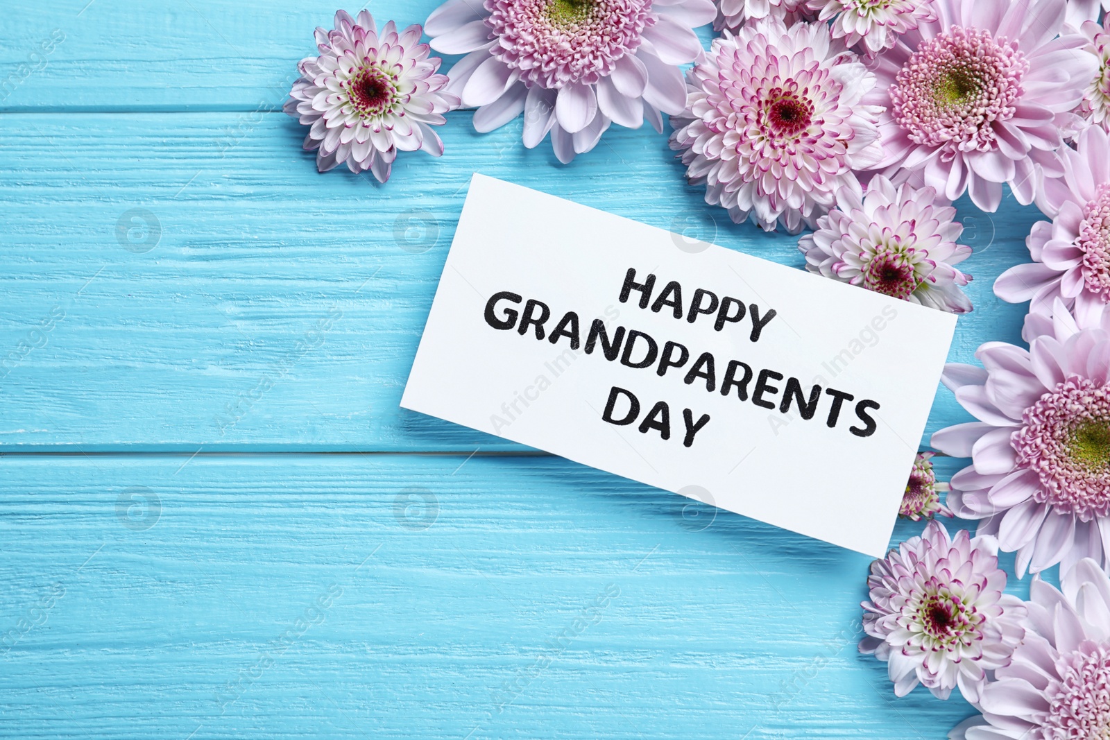 Photo of Beautiful flowers and card with phrase Happy Grandparents Day on light blue wooden background, flat lay. Space for text