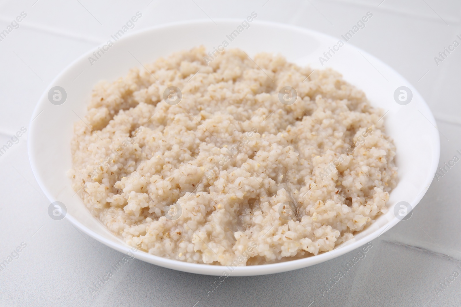 Photo of Delicious barley porridge in bowl on white table, closeup