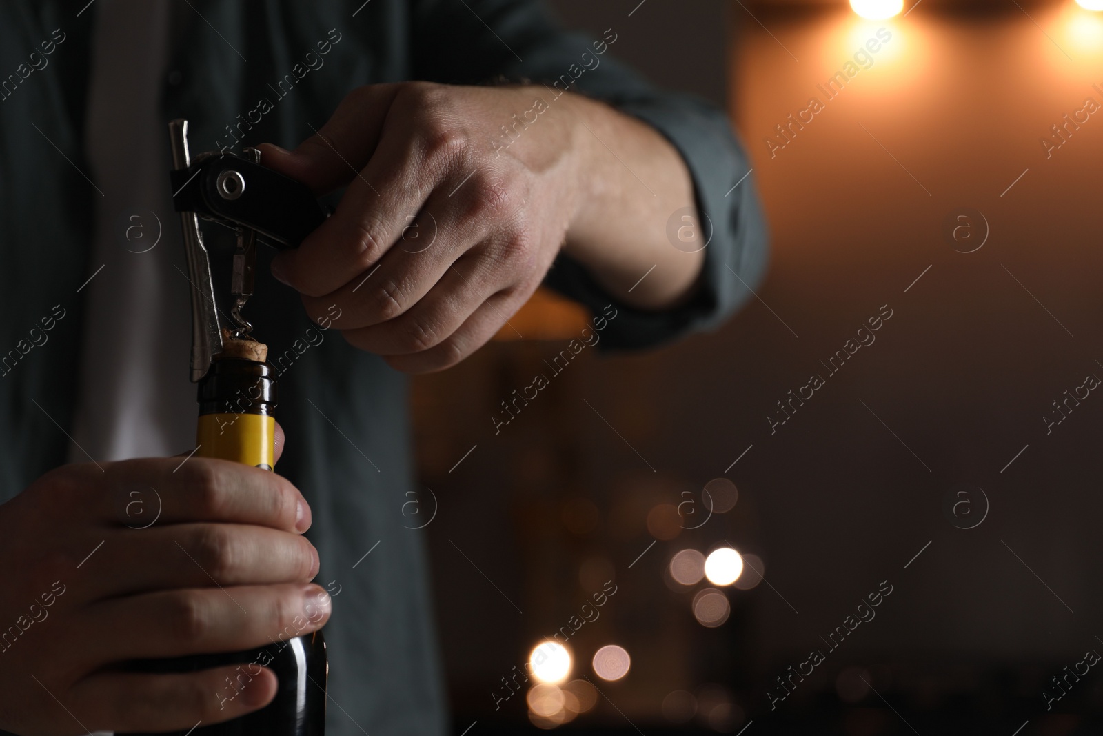 Photo of Man opening wine bottle with corkscrew on blurred background, closeup. Space for text