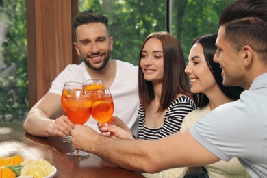 Photo of Friends clinking glasses of Aperol spritz cocktails at table