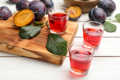 Photo of Delicious plum liquor and ripe fruits on white wooden table. Homemade strong alcoholic beverage