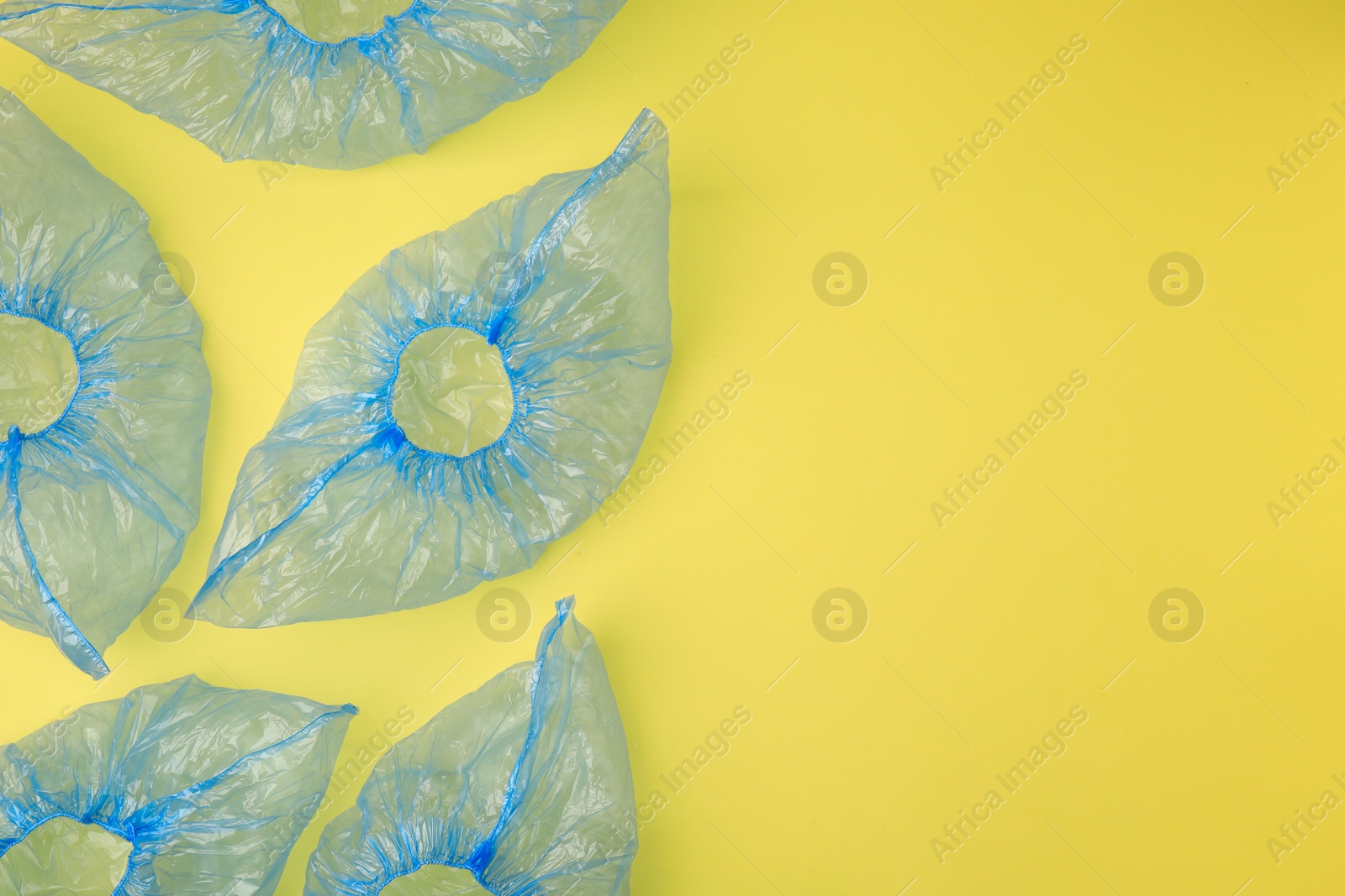 Photo of Blue medical shoe covers on yellow background, flat lay. Space for text