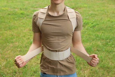 Closeup view of man with orthopedic corset on green grass outdoors