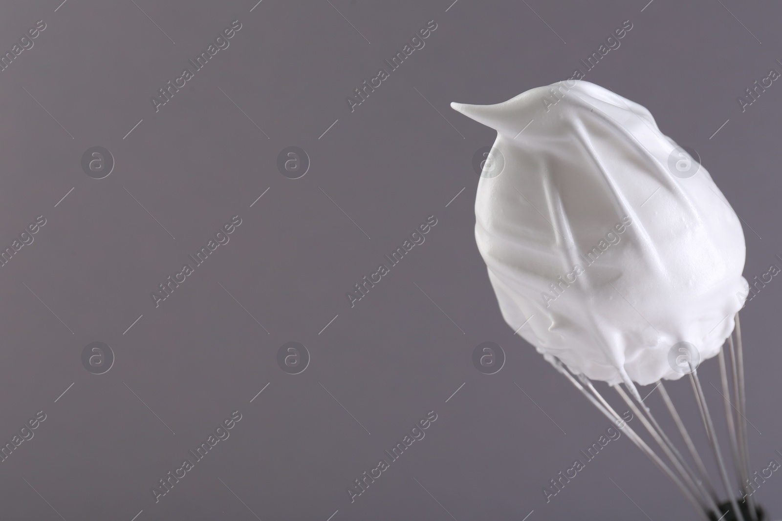 Photo of Whisk with whipped cream on grey background. Space for text