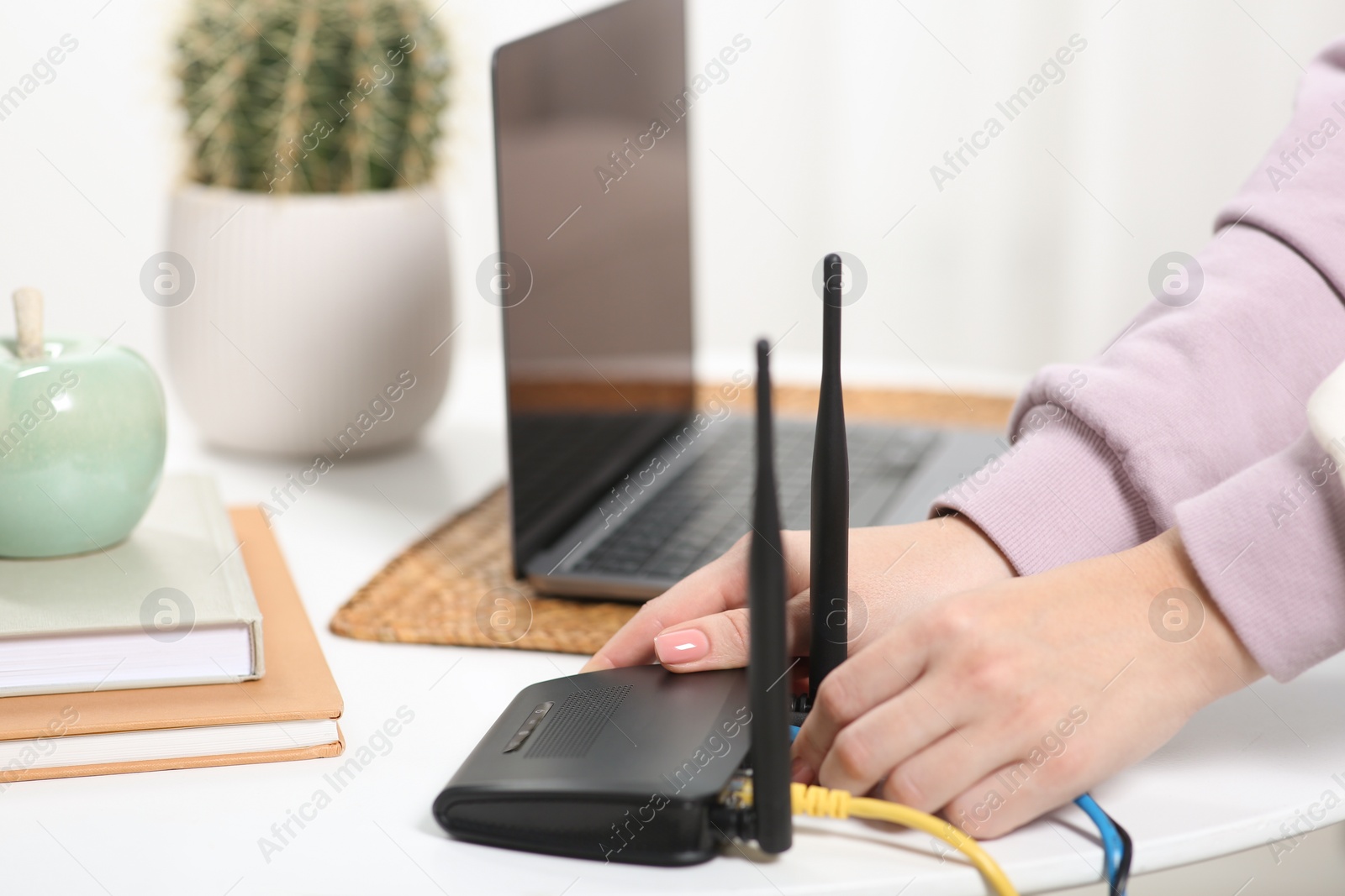 Photo of Woman connecting cable to Wi-Fi router at table indoors, closeup