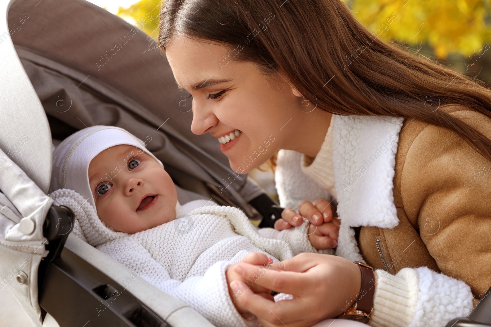 Photo of Happy mother with her baby daughter in stroller outdoors on autumn day