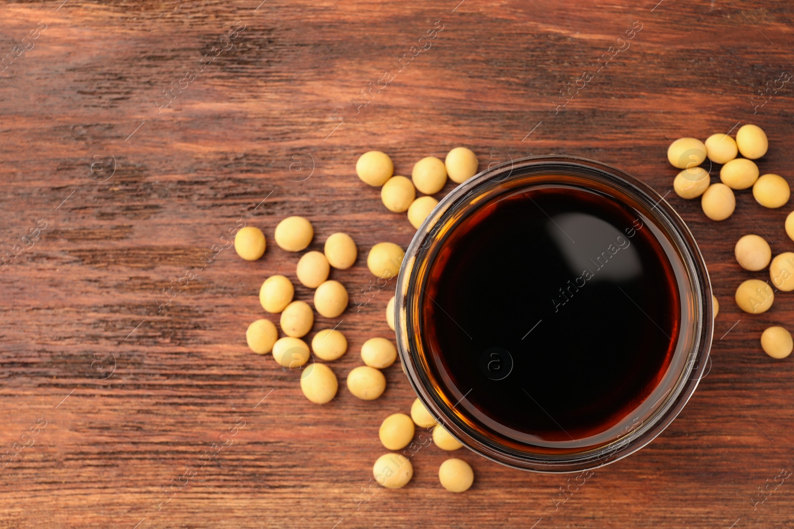 Photo of Soy sauce in bowl and soybeans on wooden table, flat lay. Space for text