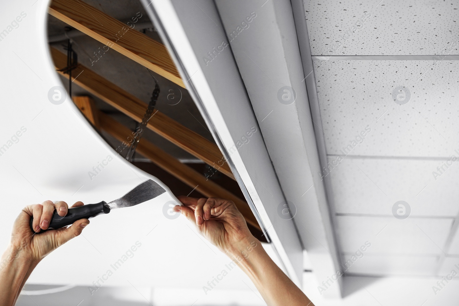 Photo of Repairman installing white stretch ceiling in room, closeup