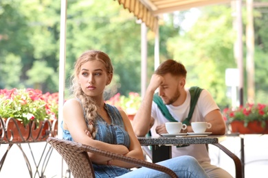Photo of Young couple arguing while sitting in cafe, outdoors. Problems in relationship
