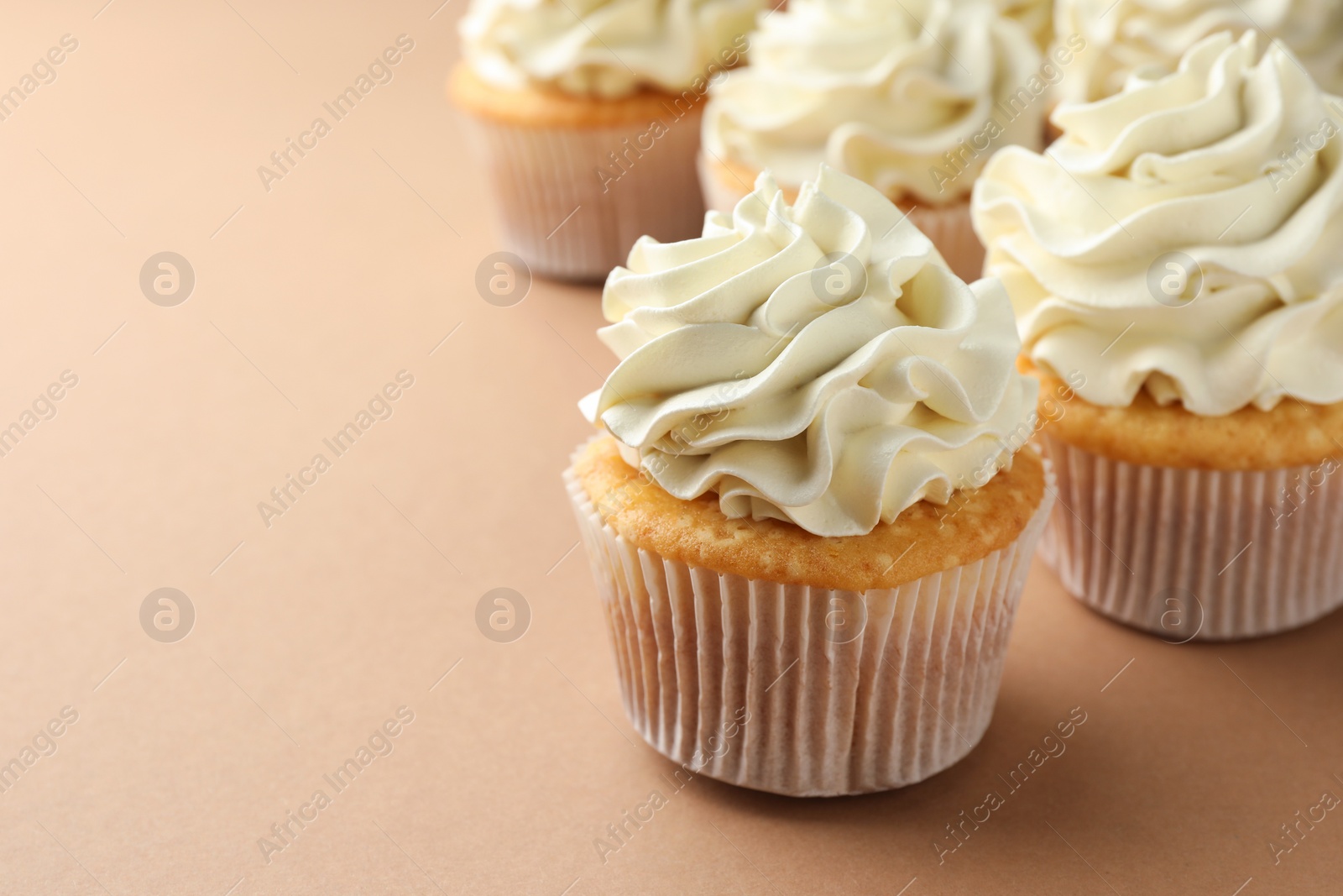 Photo of Tasty vanilla cupcakes with cream on beige table, closeup. Space for text