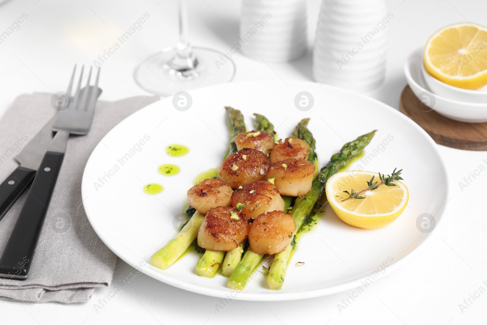 Photo of Delicious fried scallops with asparagus, lemon and thyme served on white table