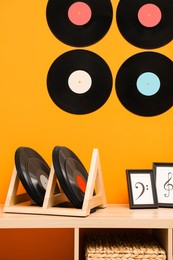 Vinyl records and pictures on wooden cabinet near orange wall