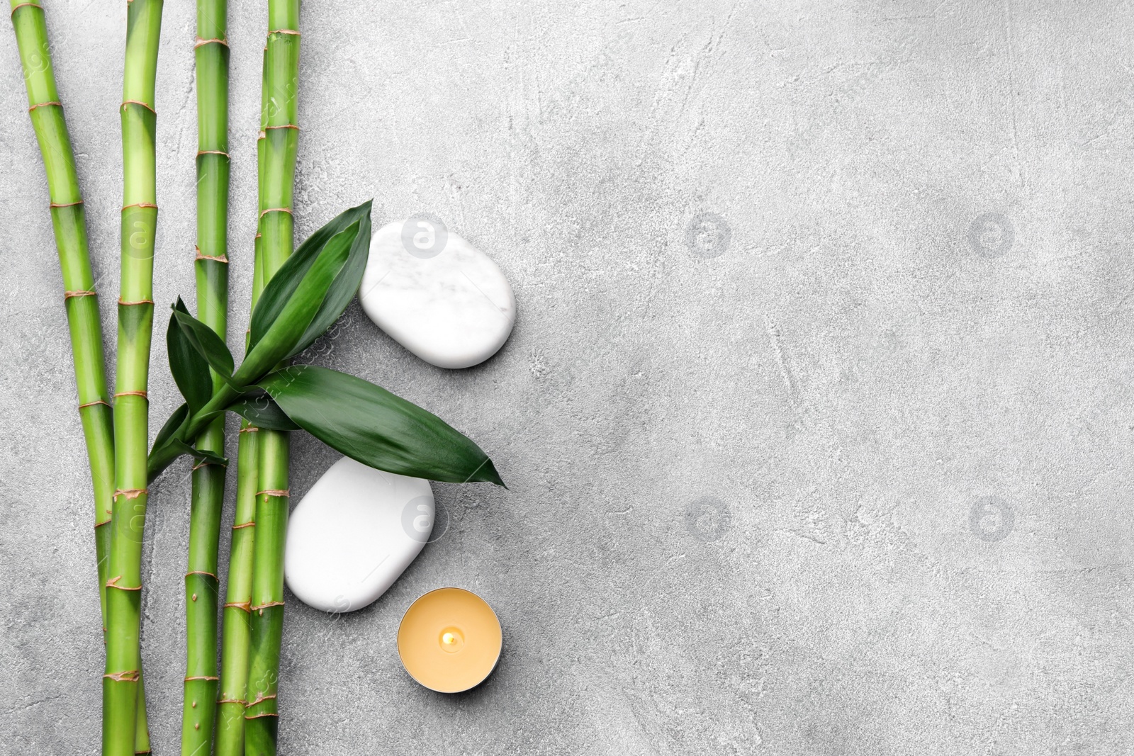 Photo of Spa stones, bamboo and burning candle on light grey table, flat lay. Space for text