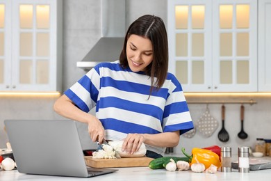 Young woman cooking while watching online course via laptop in kitchen