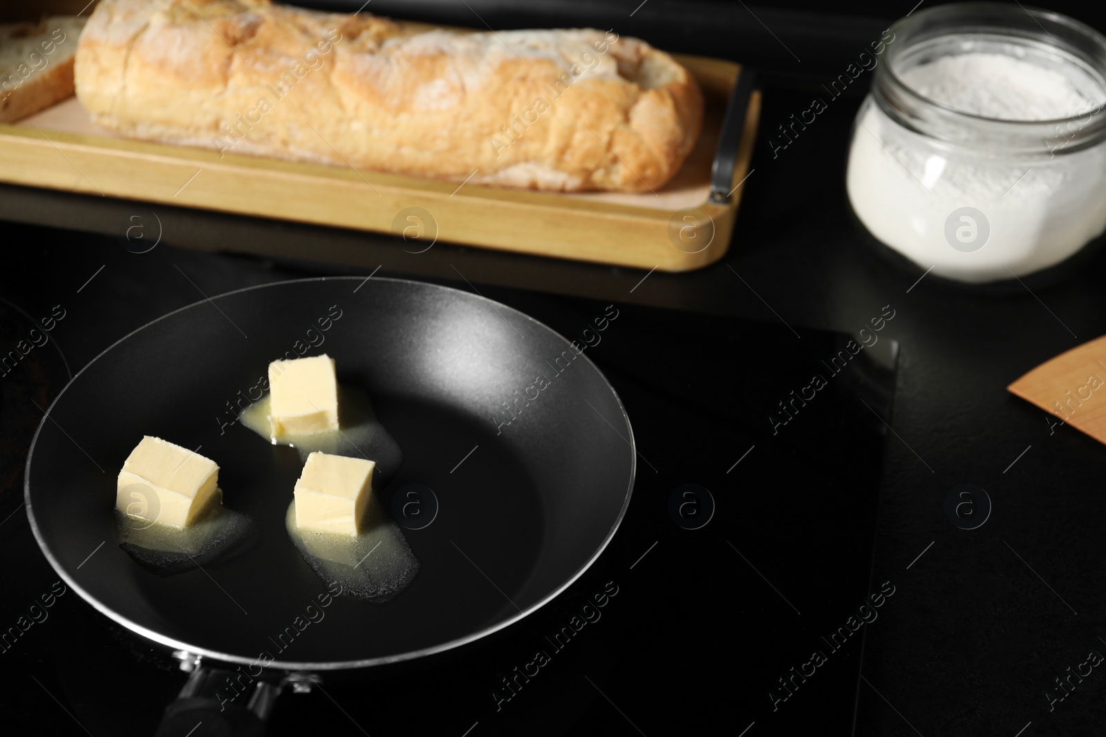 Photo of Melting butter in frying pan, bread and flour on black table