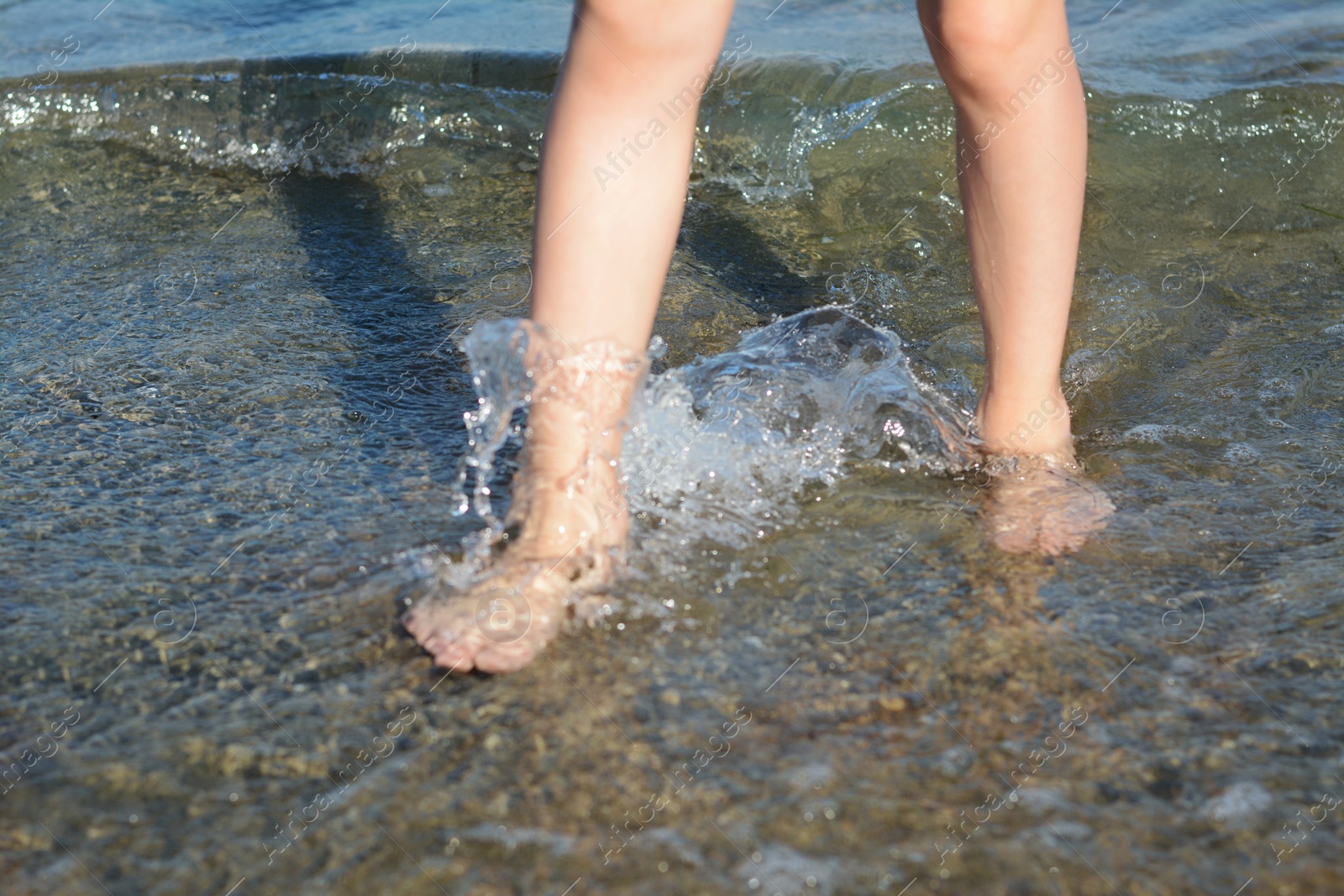 Photo of Child walking through water on seashore, closeup of legs