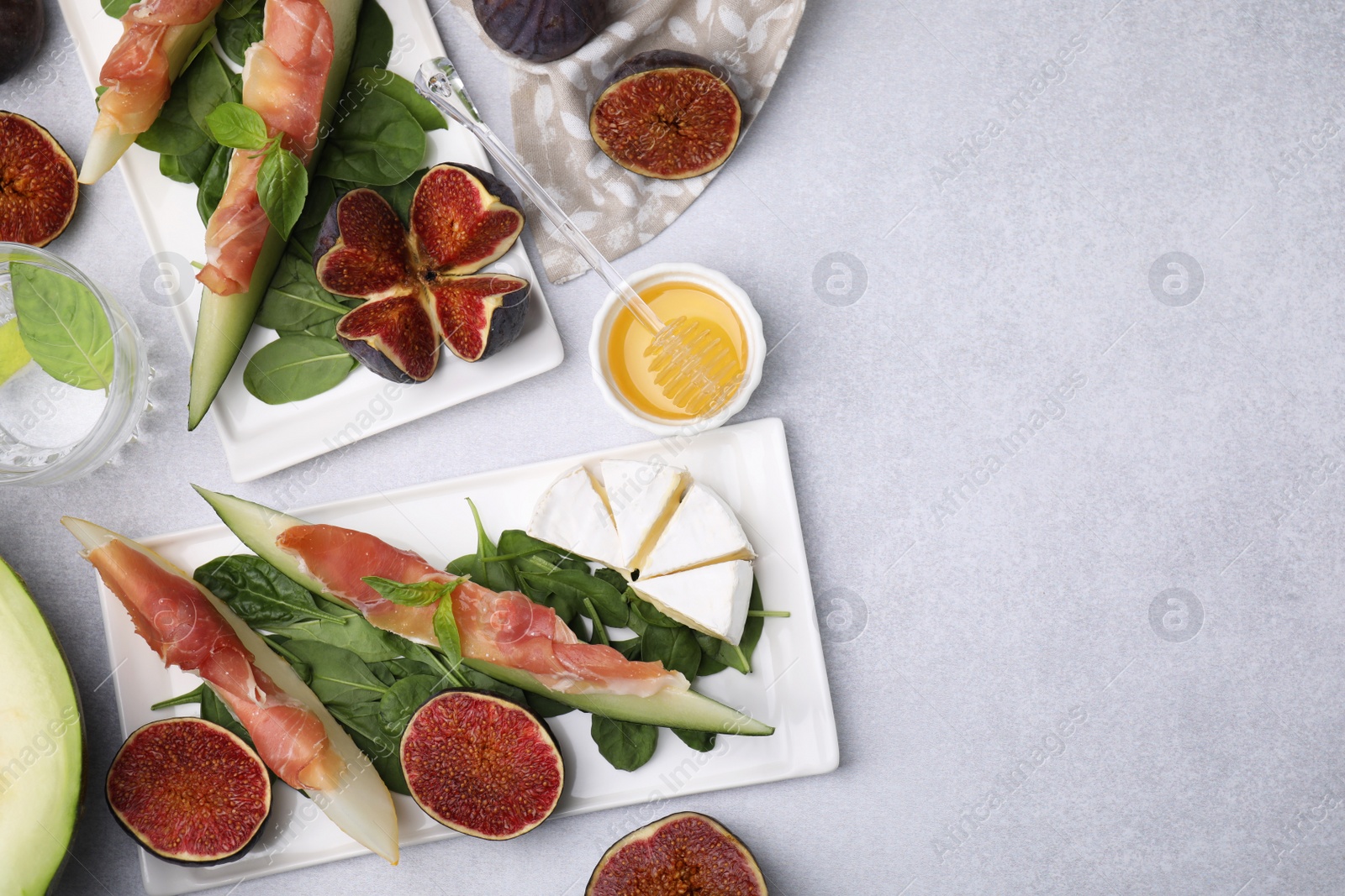 Photo of Tasty melon, jamon and figs served on light grey table, flat lay. Space for text