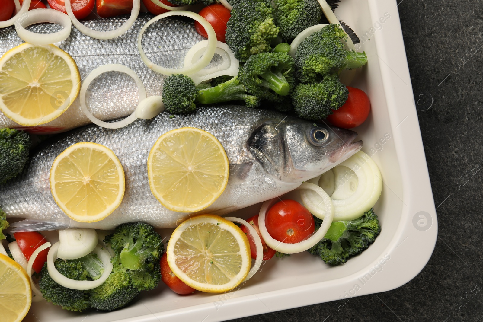 Photo of Raw fish with vegetables and lemon in baking dish on grey table, top view