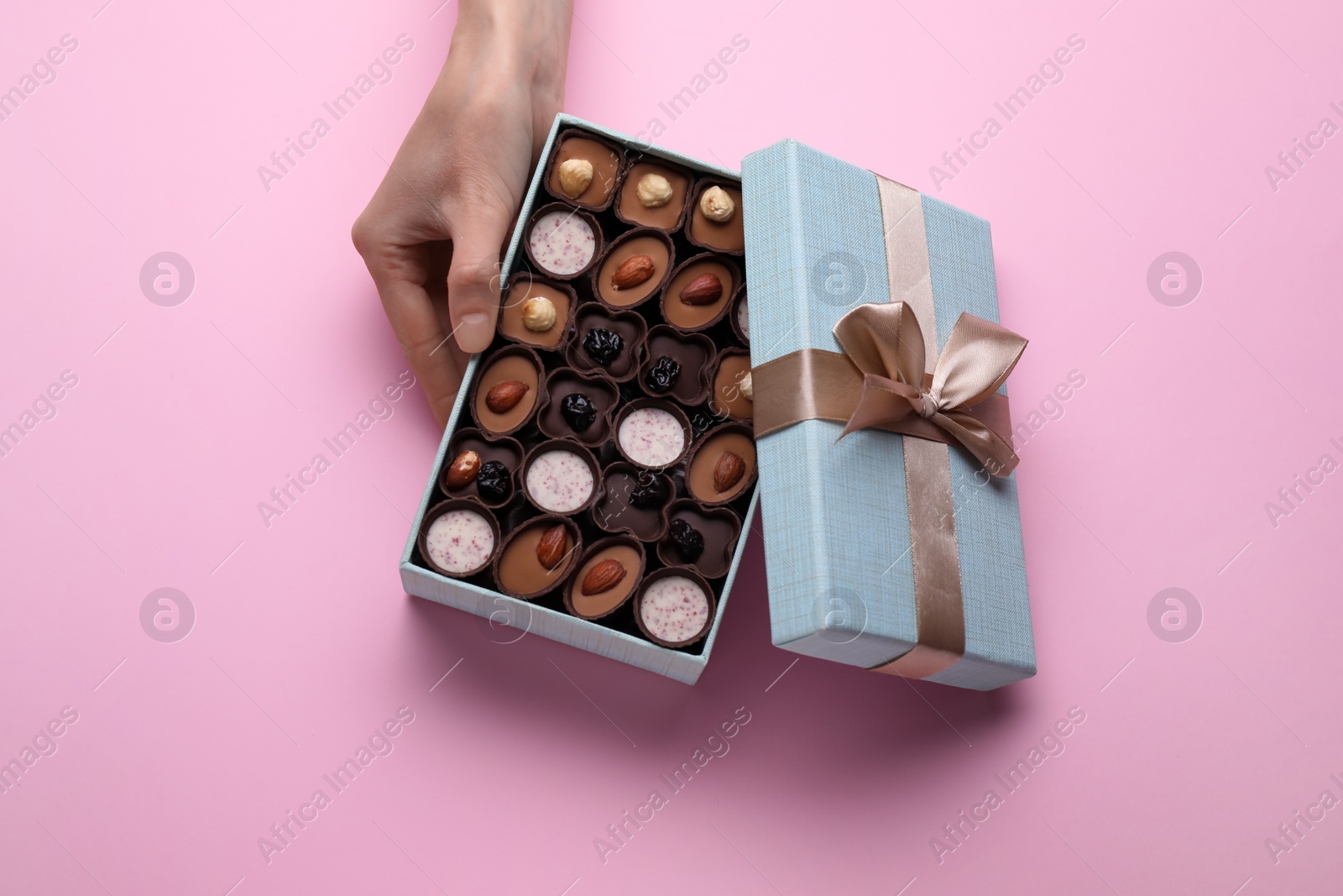 Photo of Woman with open box of delicious chocolate candies on pink background, top view