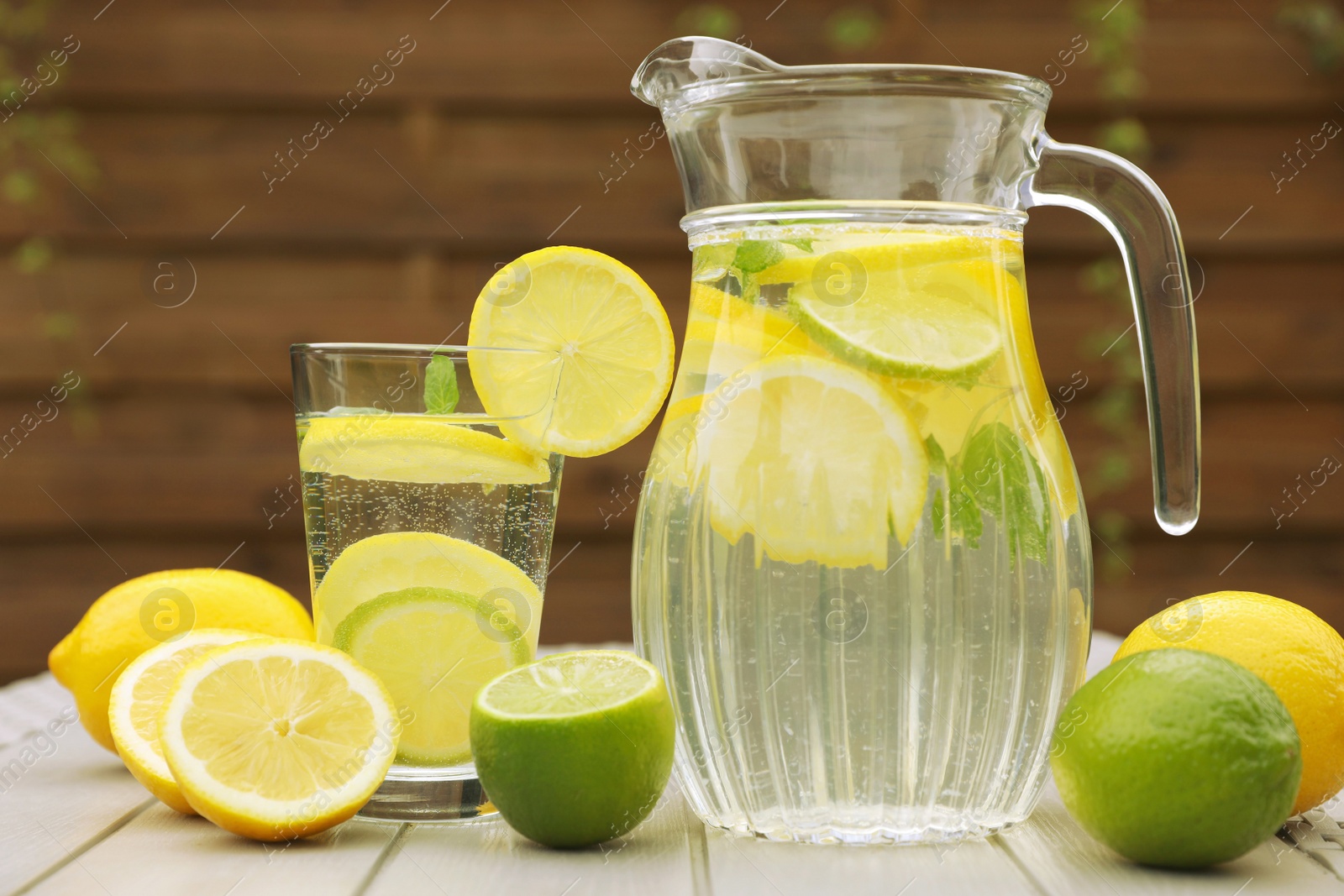 Photo of Water with lemons and limes on white wooden table outdoors