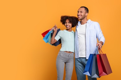Photo of Happy African American couple with shopping bags on orange background