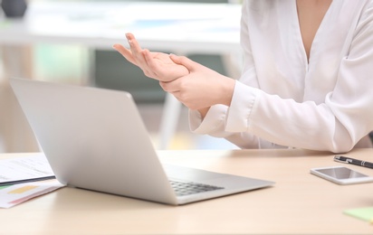 Young woman suffering from wrist pain in office