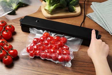 Photo of Woman packing cherry tomatoes using vacuum sealer on wooden table, closeup